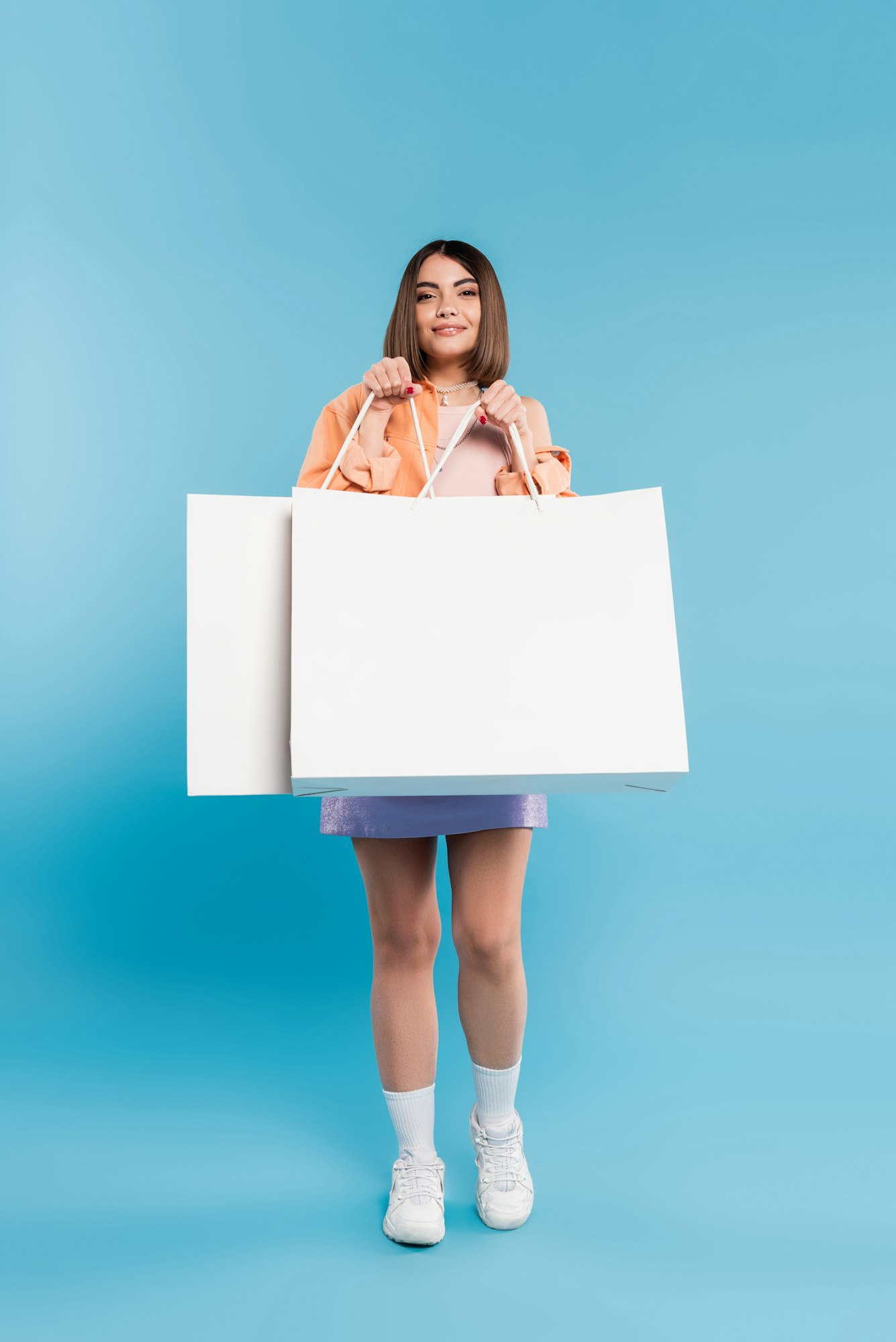 positivity, shopping spree, cheerful young woman in trendy outfit posing with shopping bags on blue